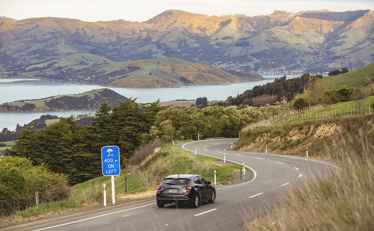 Car travelling along the scenic road toward Akaroa on Banks Peninsula, Canterbury, South Island New Zealand
