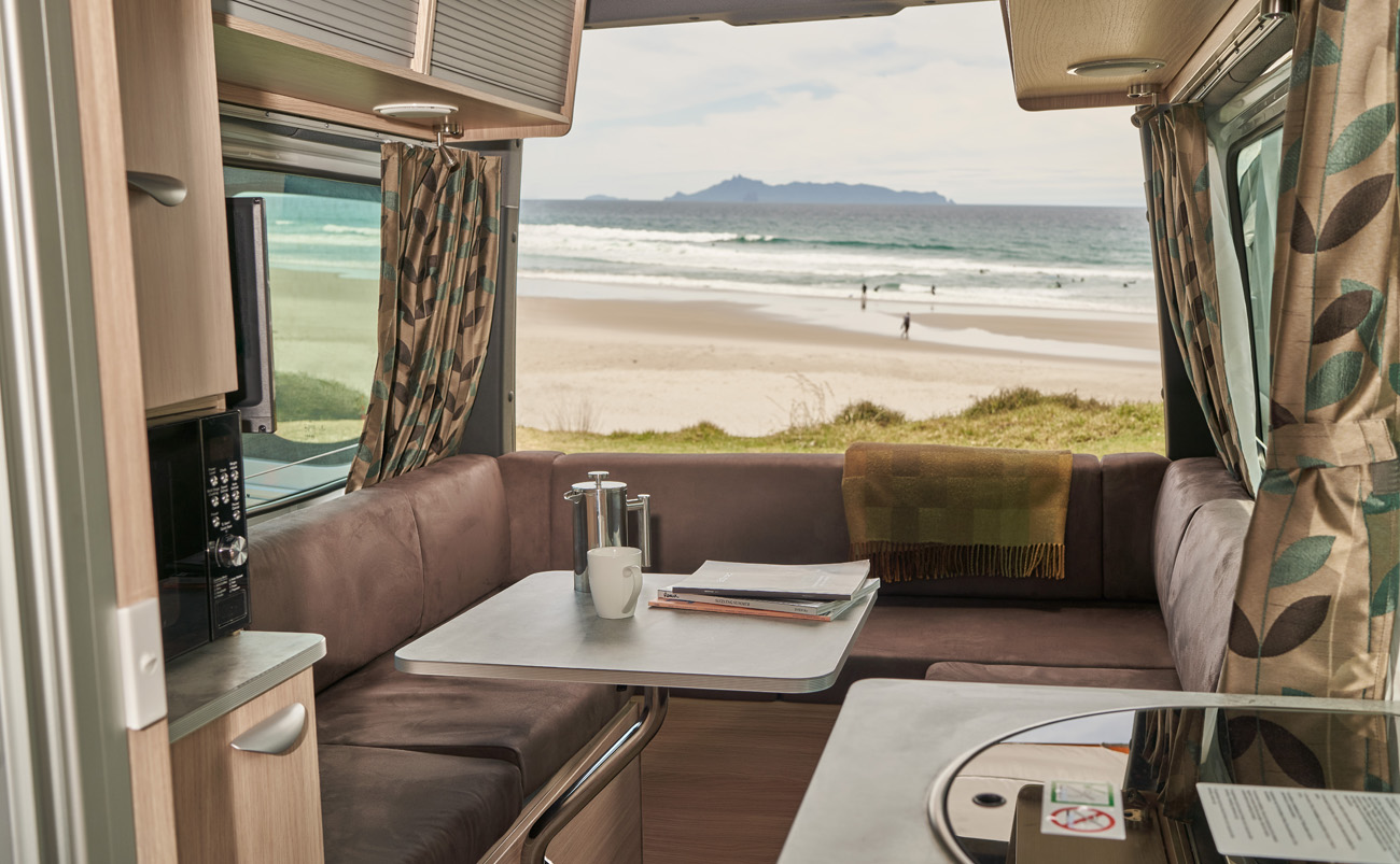 View from inside a motorhome looking through open doors towards a beach in New Zealand