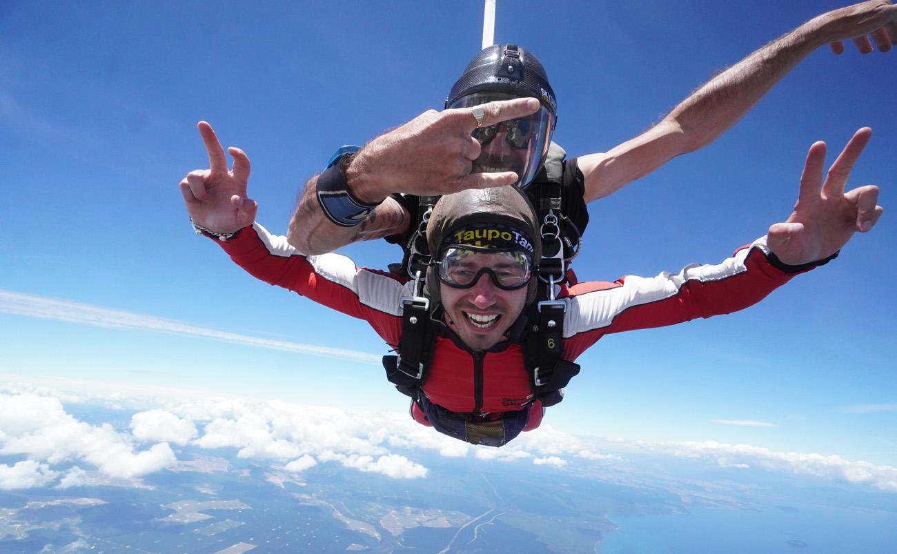 A tandem skydiver descending above Lake Taupō with volcanic mountains and the North Island landscape below
